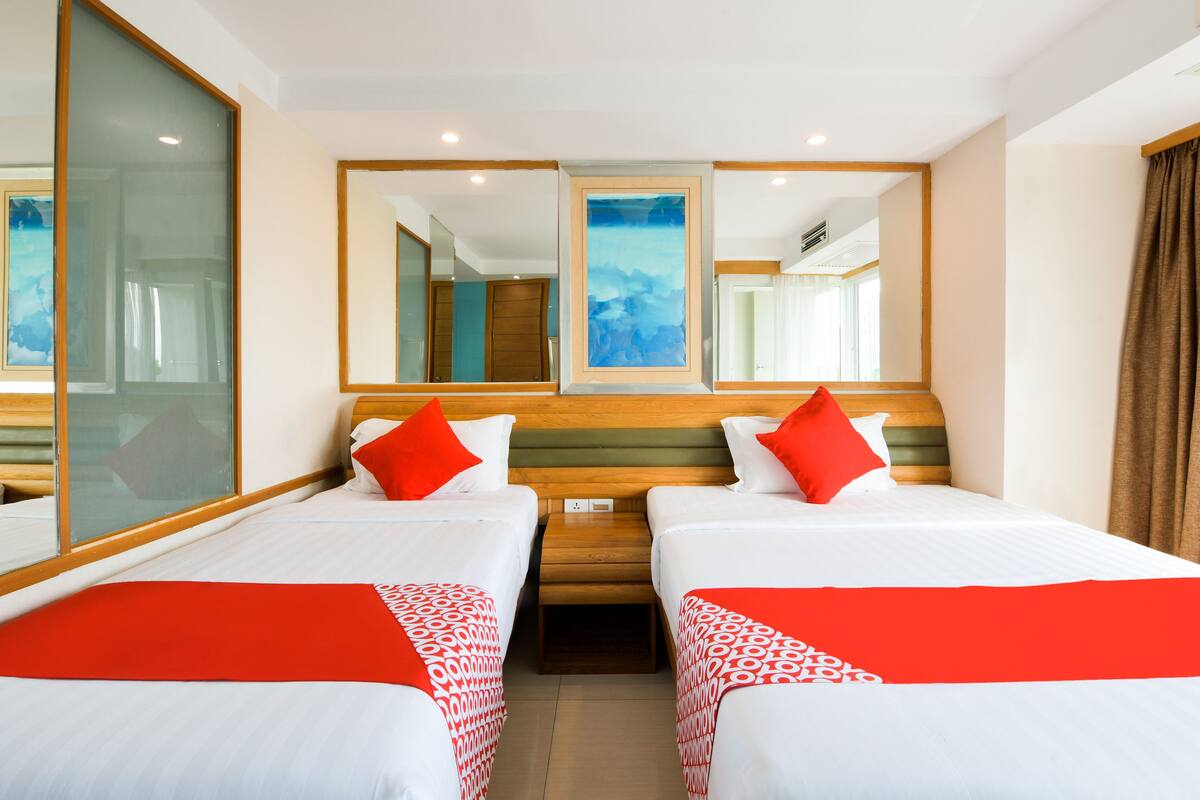 A hotel room with two beds, a large mirror, and a window.