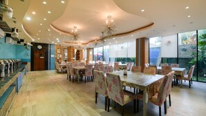 A spacious dining area with multiple tables and chairs, a counter with a display, and large windows offering a view of greenery outside. - OYO 143 Dday Resotel Pattaya Hotel (Pattaya)