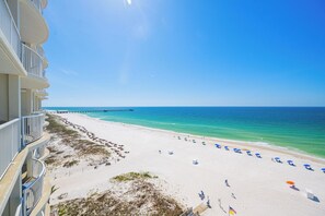 A beach view with a pier, white sand, and clear blue water.