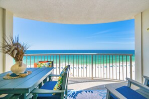 A balcony with a view of the beach, a table with a vase, and a chair with a cushion.