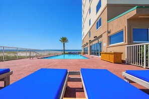 A pool area with blue lounge chairs, a palm tree, and a building with large windows.