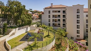 A residential building with a courtyard featuring a playground, a staircase, and a garden with various plants.