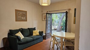 A cozy room with a dark green sofa, a small round table, and a door leading to an outdoor area with a tree and a fence. - Arrábida Sea & Country side Villa (Azeitão)