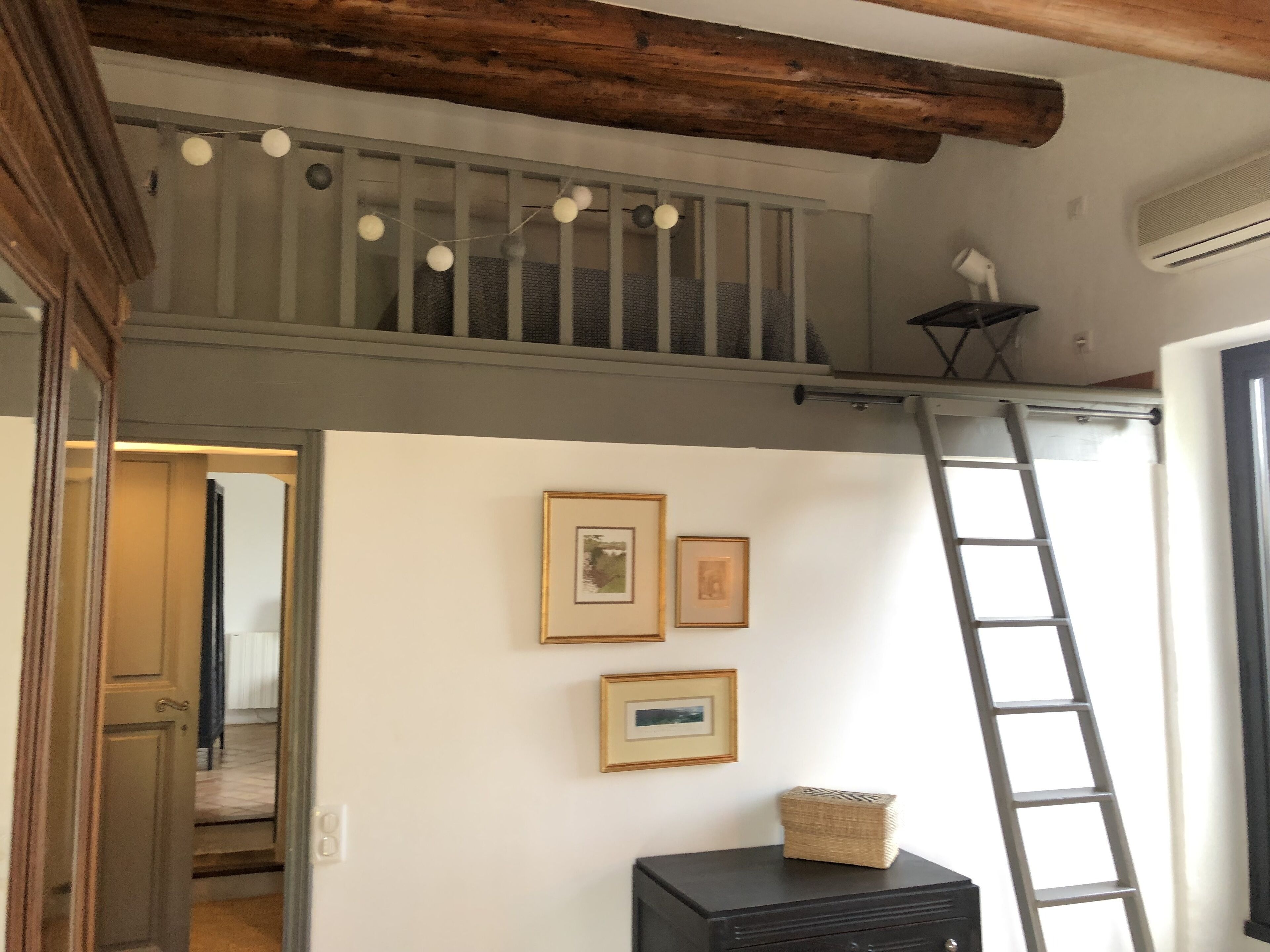 A room with a loft area, a ladder, and a black cabinet with a basket on top.