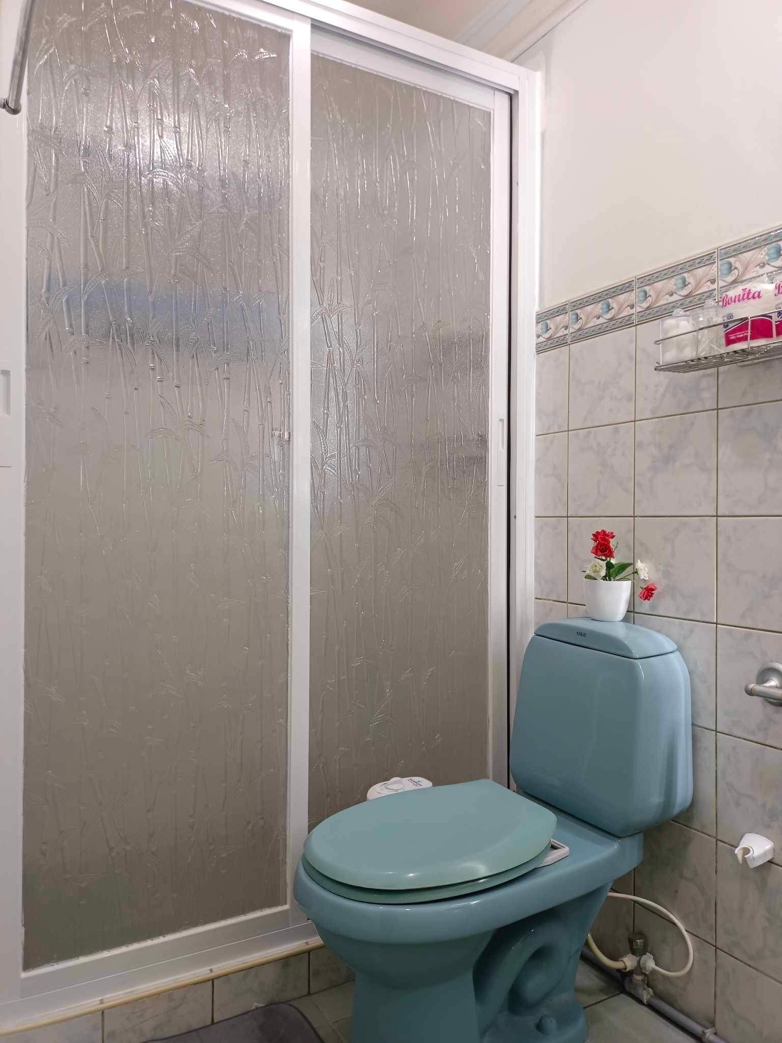Un baño con inodoro, cabina de ducha de vidrio y pared con azulejos.