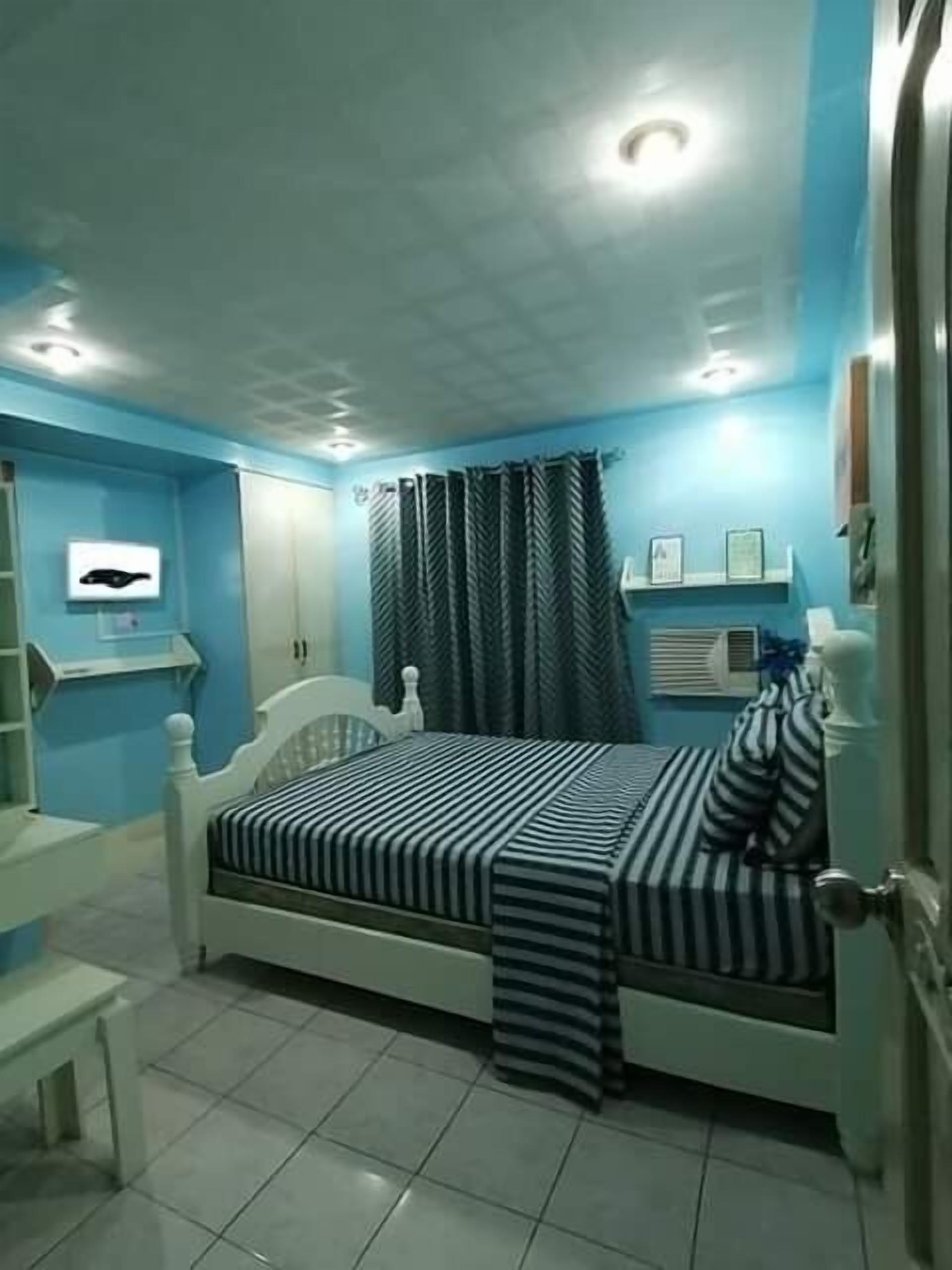 Un dormitorio con cama, cortinas y una estantería con cuadros enmarcados.