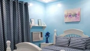 Un dormitorio con cama, cortinas, mesita de noche, un reloj de pared y un cuadro enmarcado.