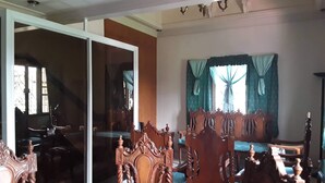Amplia sala de estar con un sofá grande de madera, una mesa de comedor con sillas y un puerta corrediza de vidrio que da a otra habitación.