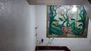 Un escalier avec une rampe en bois, un vase bleu contenant des plantes et une fenêtre à vitraux ornée de motifs floraux.
