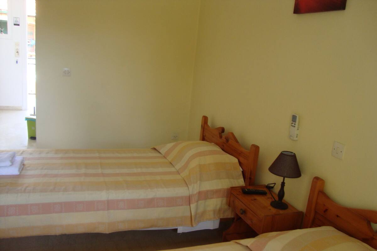 Une chambre avec deux lits, chacun doté de draps à rayures, une table de chevet avec une lampe et une prise électrique au mur.