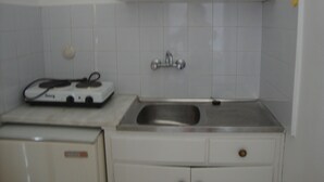 A kitchen with white cabinets, a stainless steel sink, and a small refrigerator. - Anya Studios (Corfu)