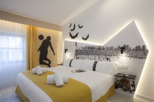 A hotel room with a bed, a nightstand, a wall mural, and a window with curtains.