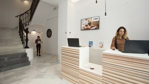 A reception area with a reception desk, a staircase, and a mounted television displaying a commercial. - Casual Socarrat Valencia Hotel by Casual Hoteles (Valencia)