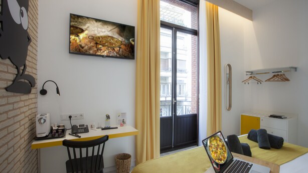 A hotel room with a desk, a bed, a laptop, a chair, a window with curtains, a wall-mounted TV, and a small trash bin. - Casual Socarrat Valencia Hotel by Casual Hoteles (Valencia)