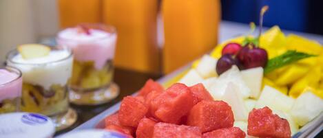 A variety of fruits and beverages on a tray, including watermelon, pineapple, and grapes, with a blurred background of bottles.