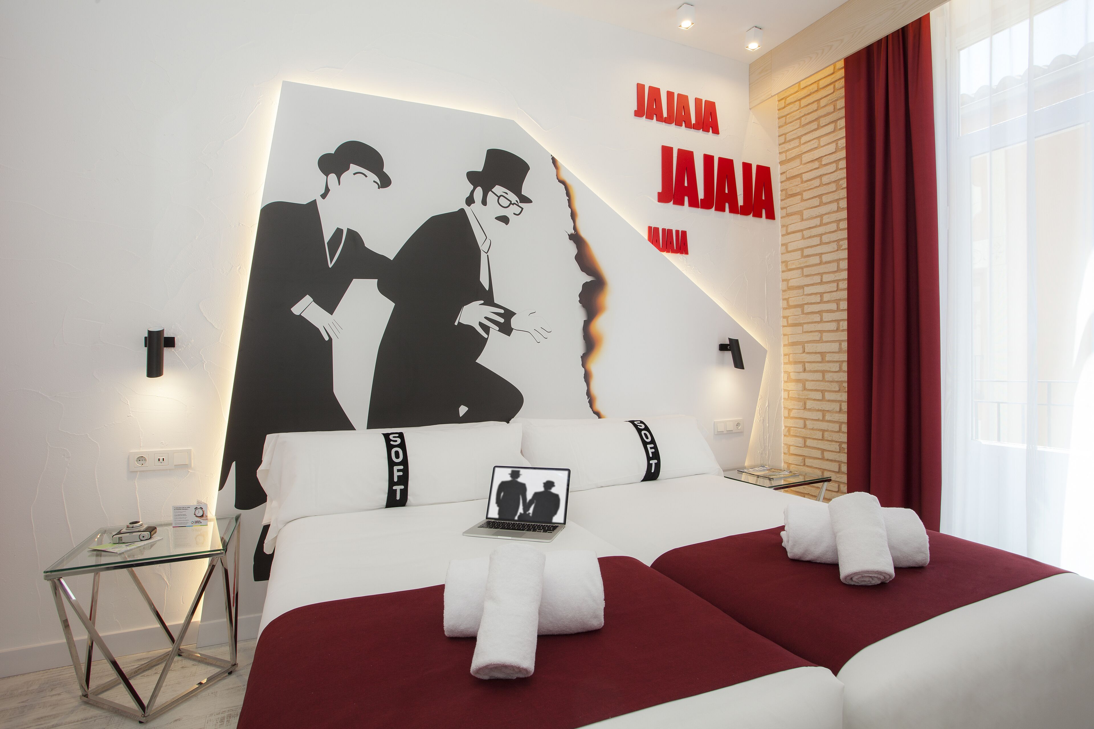 Camera d'albergo con un letto, un tavolino in vetro, un portatile e un grande affresco sulla parete.