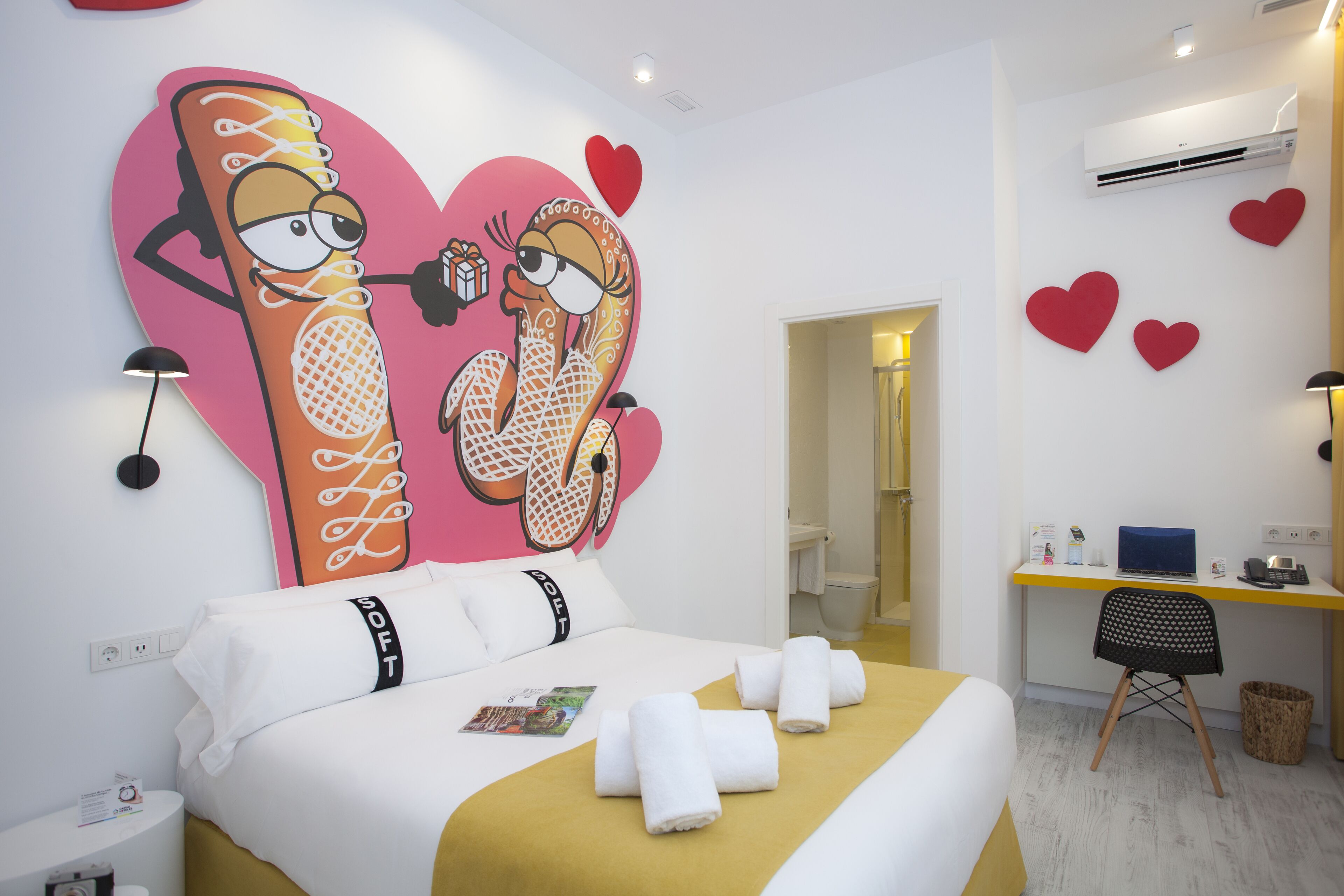 Habitación de hotel con una cama, un escritorio y una pared decorada con corazones.