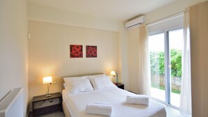 A hotel room with a large bed, two bedside tables with lamps, a window with curtains, and two wall-mounted artworks. - Nopigia Mare Villa (Kissamos)
