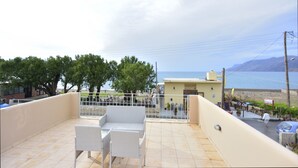 A balcony with white wicker furniture, a view of the sea, and a building in the background. - Nopigia Mare Villa (Kissamos)