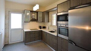 A modern kitchen with stainless steel appliances, wooden cabinets, and a built-in oven. - Nopigia Mare Villa (Kissamos)