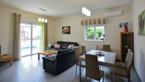 A spacious living area with a sofa, dining table, and chairs. There is a sliding glass door leading to a balcony. - Nopigia Mare Villa (Kissamos)