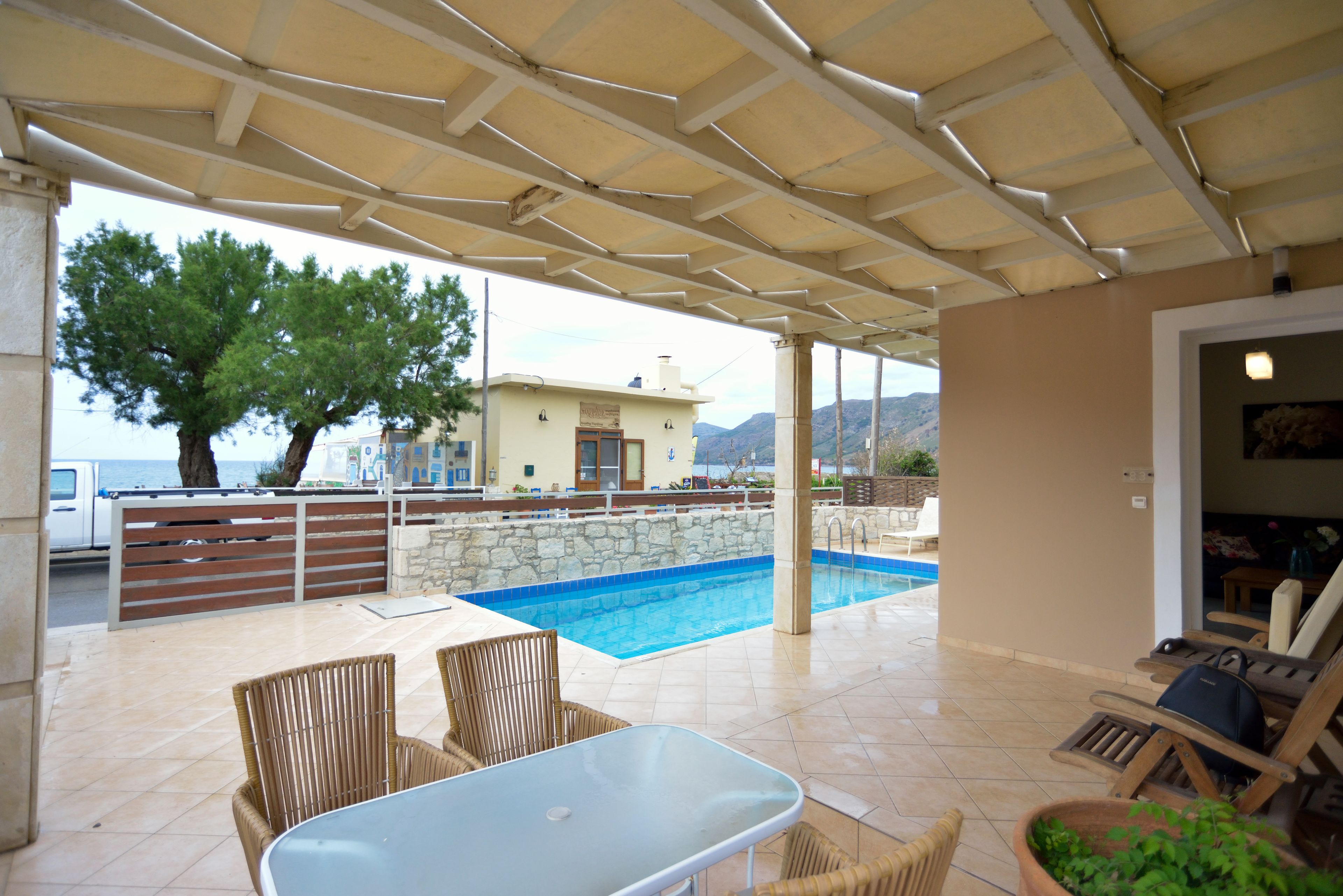 An outdoor pool area with a covered patio, lounge chairs, and a table.