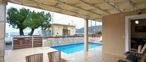 An outdoor pool area with a covered patio, lounge chairs, and a table.