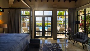 A hotel room with a bed, a sofa, a coffee table, a chair, and a view of an outdoor pool area. - STUNNING Villa w/Infinity Pool& Outdoor Kitchen! Across from Marriott! (Noord)