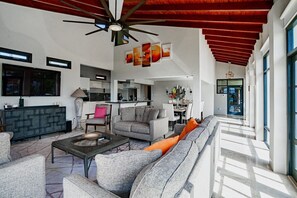 A spacious living area with a modern kitchen, a dining area, and a large sofa with orange cushions. - STUNNING Villa w/Infinity Pool& Outdoor Kitchen! Across from Marriott! (Noord)