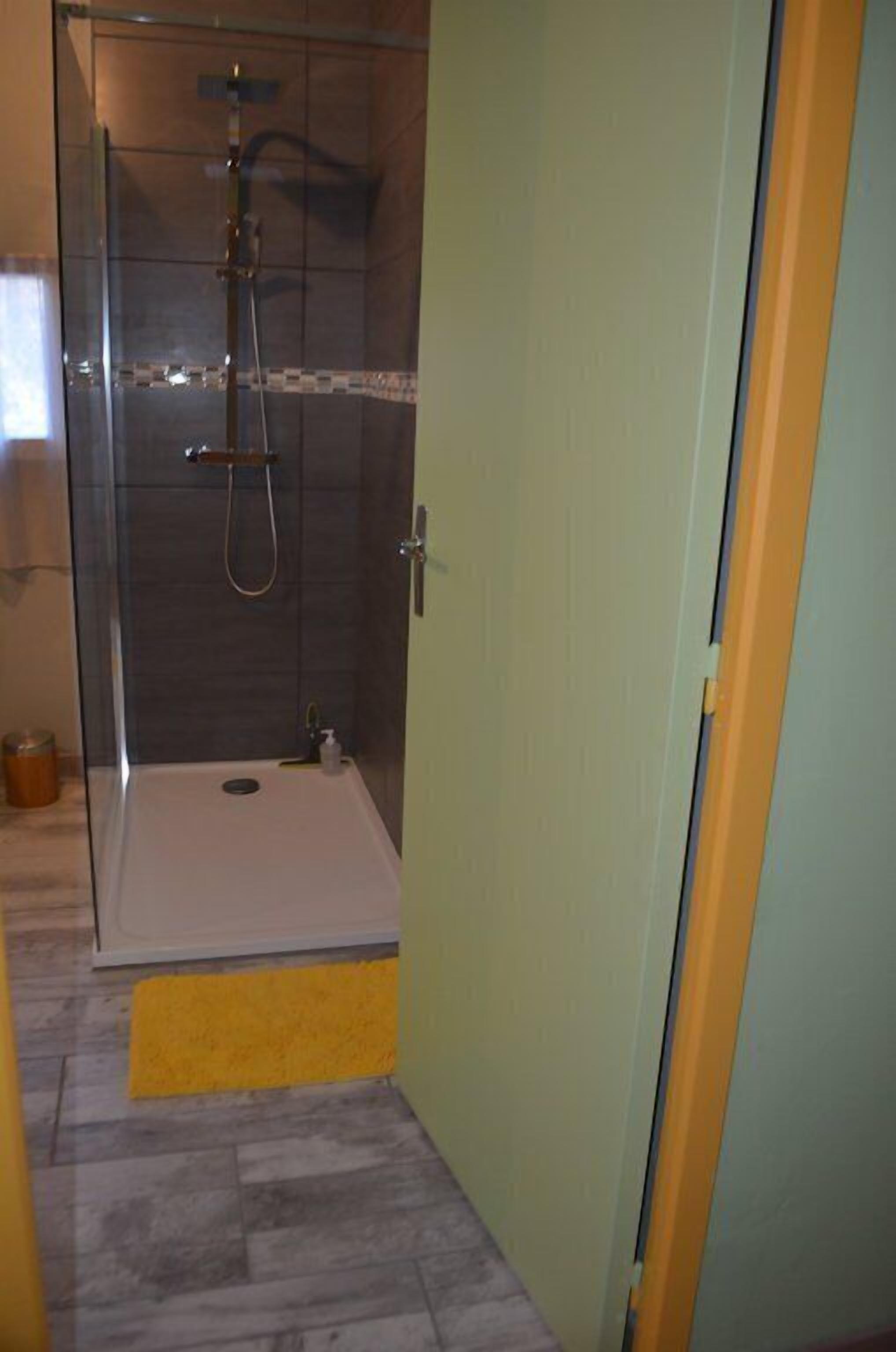 A glass-enclosed shower area with a white bathtub, a yellow mat, and a tiled floor.