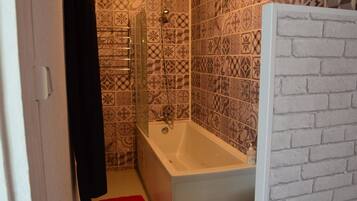 Une salle de bain avec des carreaux décorés, une baignoire, une douche et un mur d’accent en briques blanches.