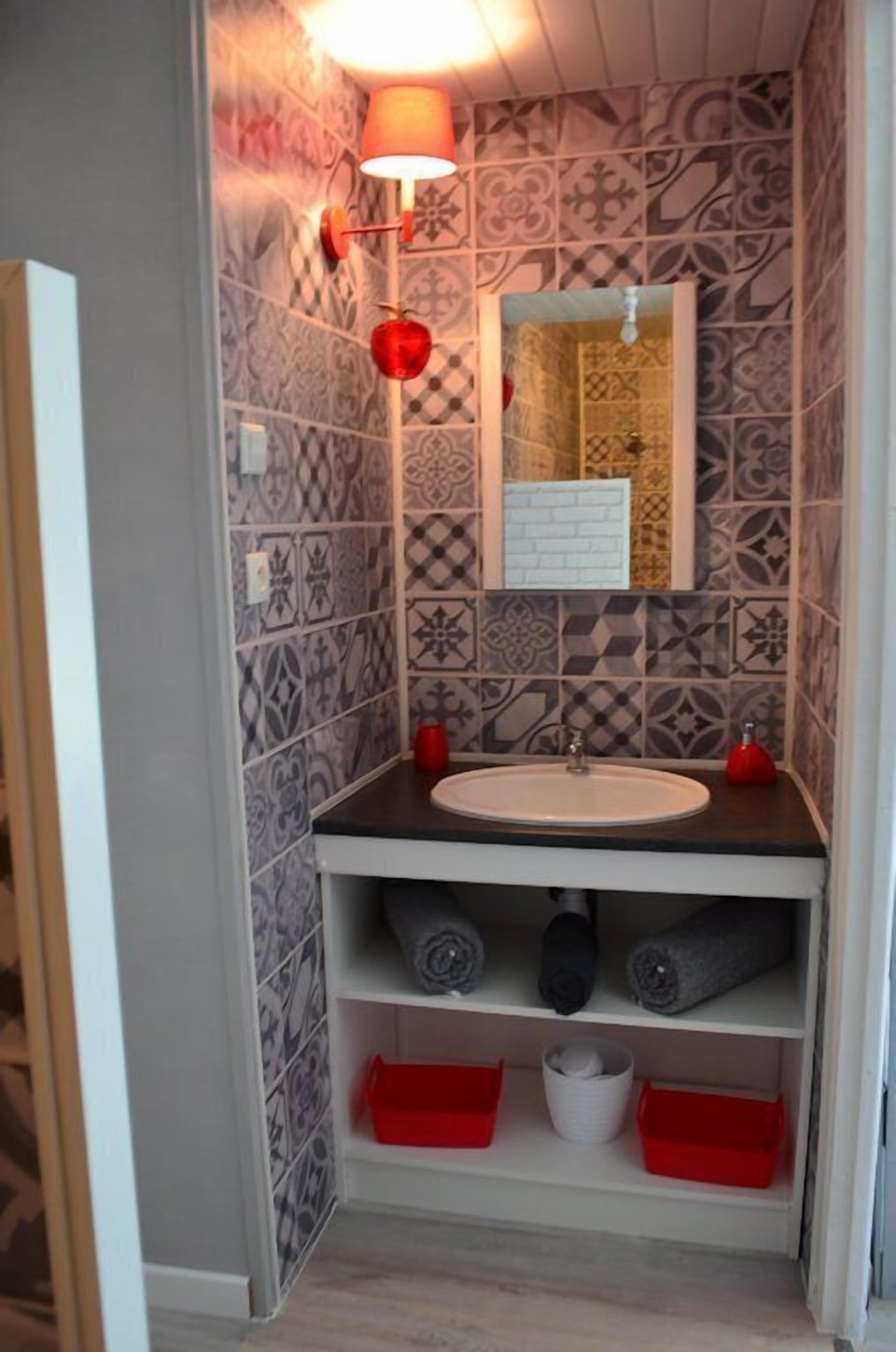 A bathroom with patterned tiles, a white sink, a mirror, and shelves with towels and red baskets.