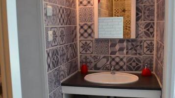 A bathroom with patterned tiles, a white sink, a mirror, and shelves with towels and red baskets.