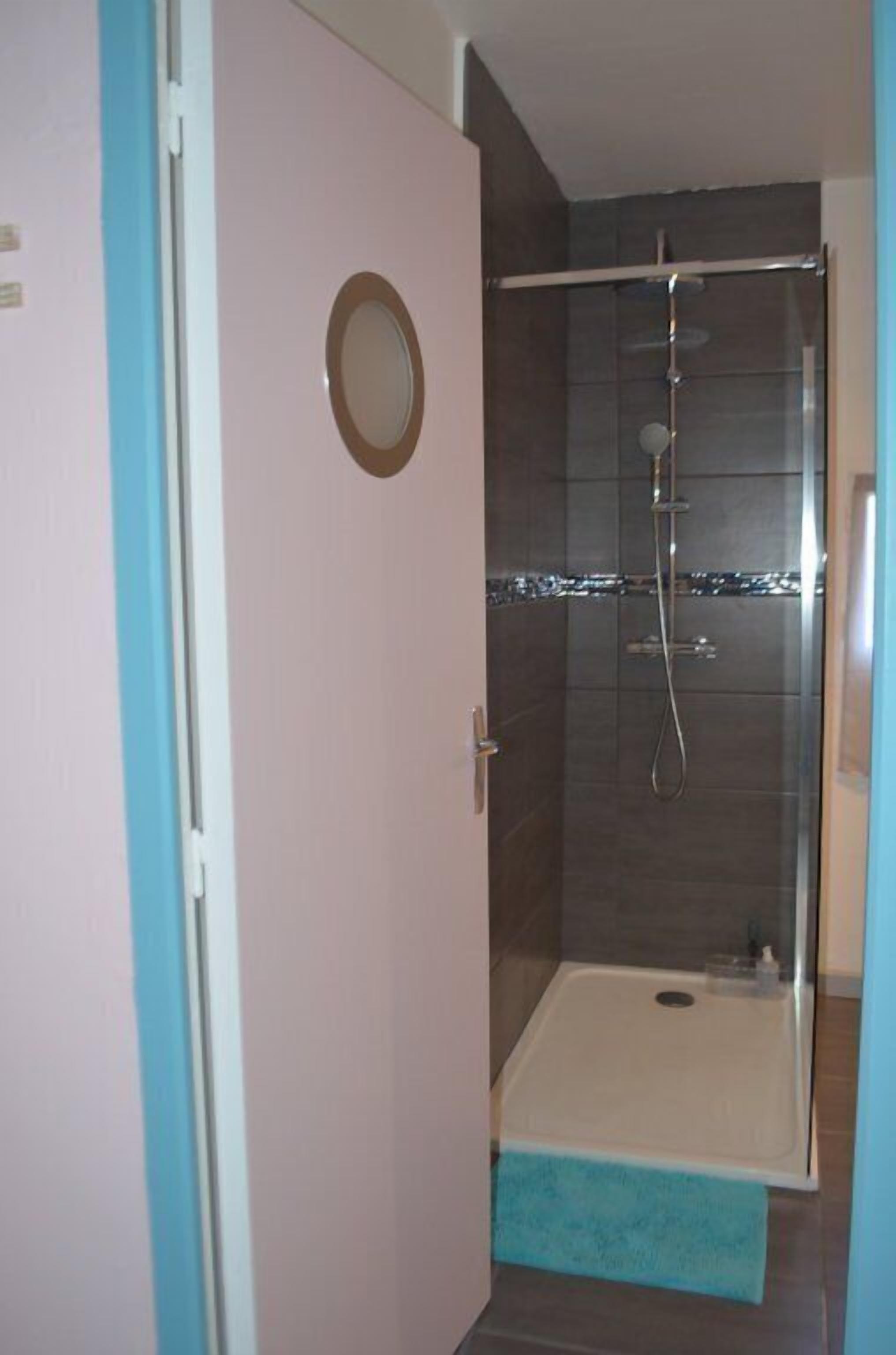 Un baño con cabina de ducha de vidrio, bañera blanca y una alfombra azul.