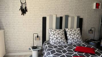 Une chambre moderne avec un mur en briques blanches, un lit avec une literie à motifs géométriques et un attrape-rêves accroché au mur.