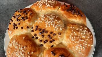 A plate of bread rolls with chocolate chips and nuts, two red cups of coffee, and a dark grey table.