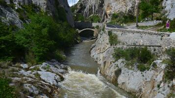 Ein Fluss fließt unter einer Steinbrücke, rechts davon verläuft eine Straße.