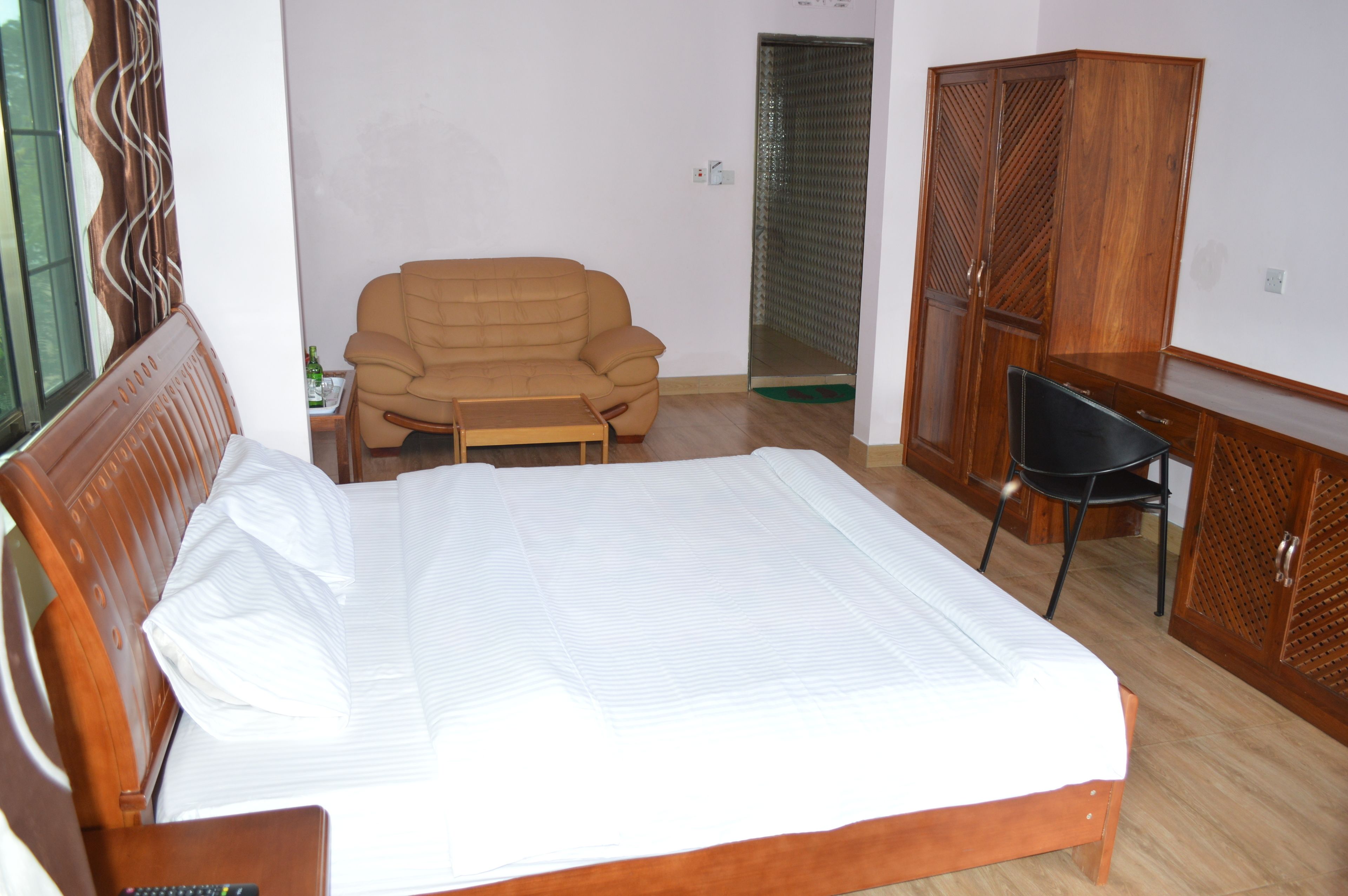 A bedroom with a bed, a wooden wardrobe, a wooden desk, a chair, and a sofa.