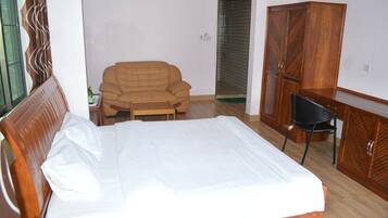 A bedroom with a bed, a wooden wardrobe, a wooden desk, a chair, and a sofa.