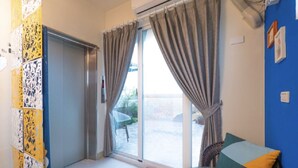 A room with a sliding glass door leading to a balcony, a small table with a remote control, and a chair.