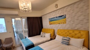 A hotel room with two beds, a chandelier, a painting on the wall, and a view through the window.