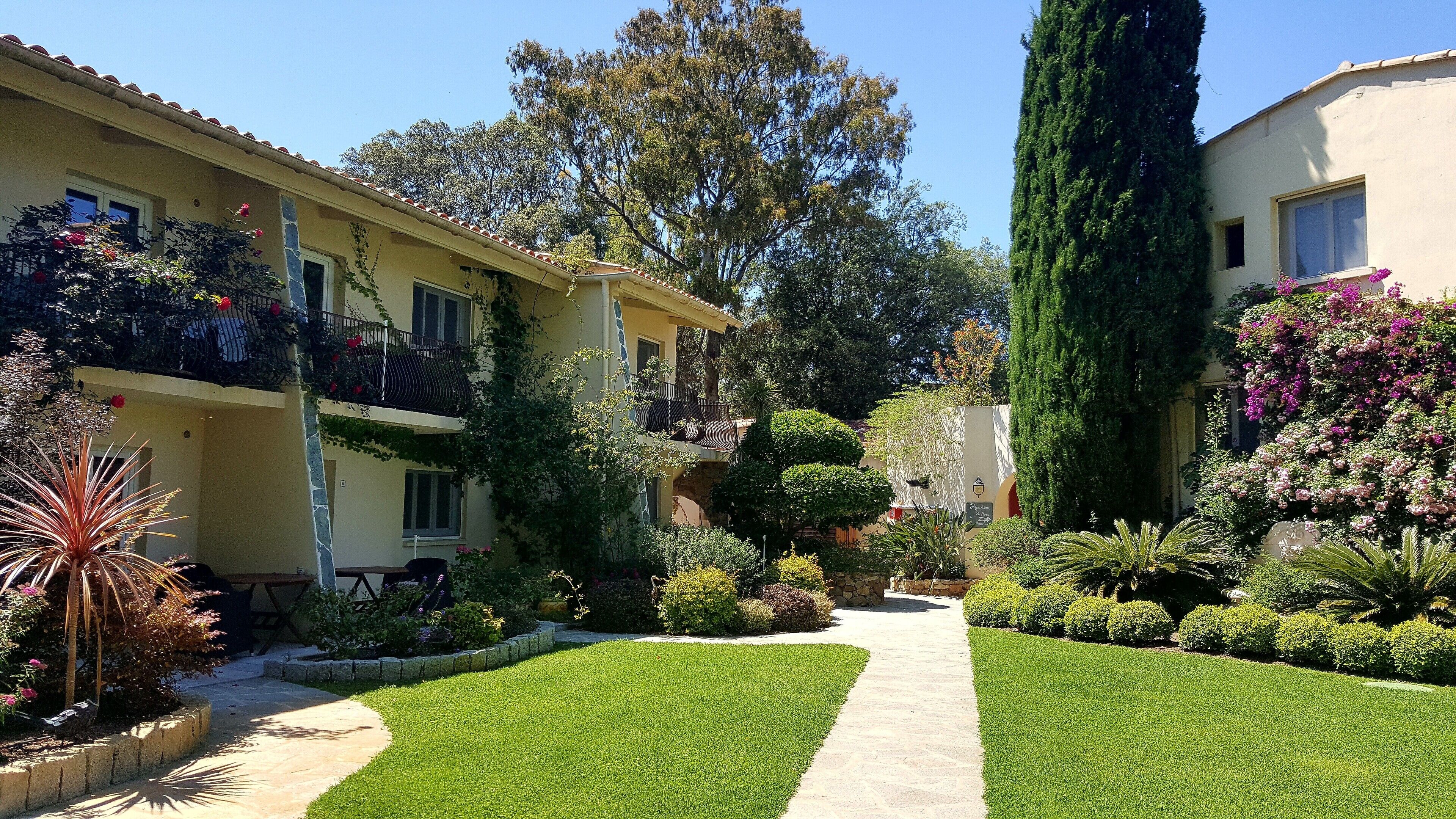A residential building with a well-maintained garden, a paved pathway, and a balcony with a railing.
