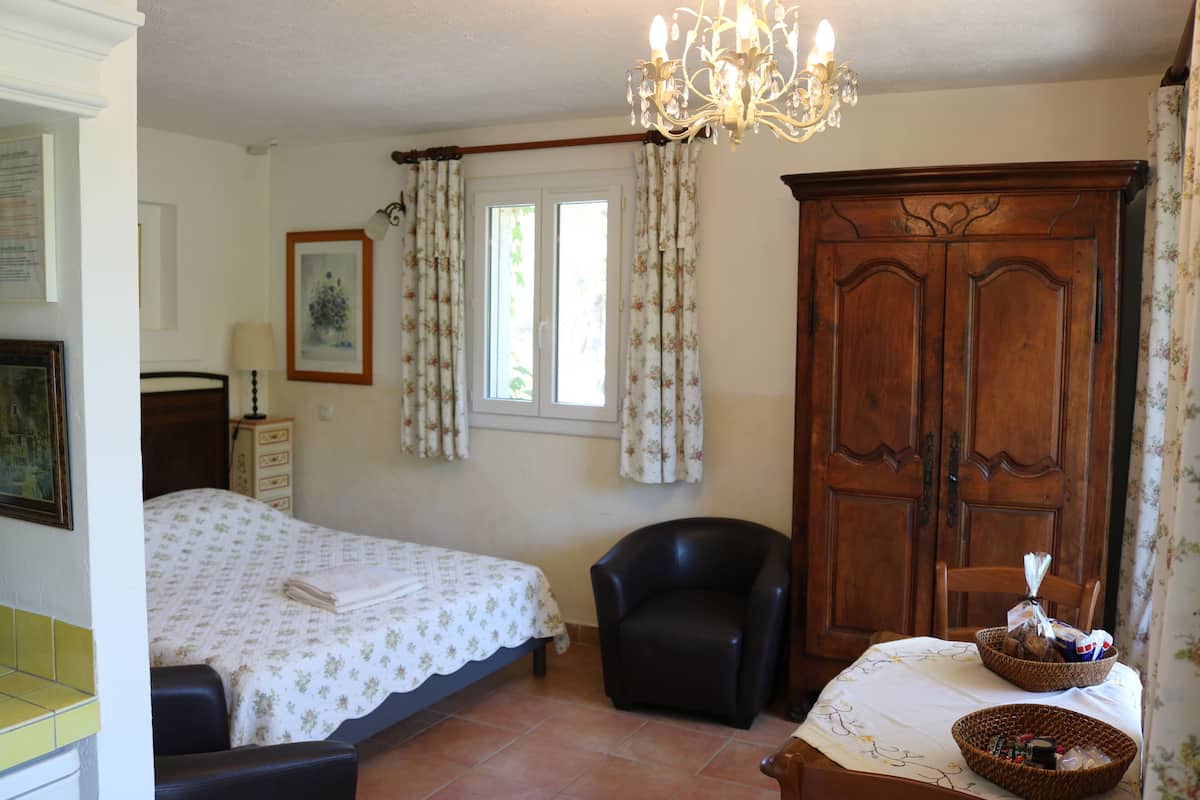 Une chambre à coucher comprenant un lit, une chaise, une armoire en bois, un lustre et une fenêtre avec des rideaux.