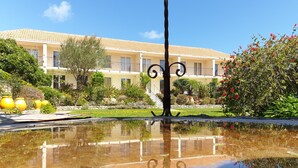 A courtyard with a reflective pool, a building with a tiled roof, and a variety of plants and flowers. - Résidence Le Home (Calvi)