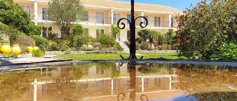 A courtyard with a reflective pool, a building with a tiled roof, and a variety of plants and flowers.