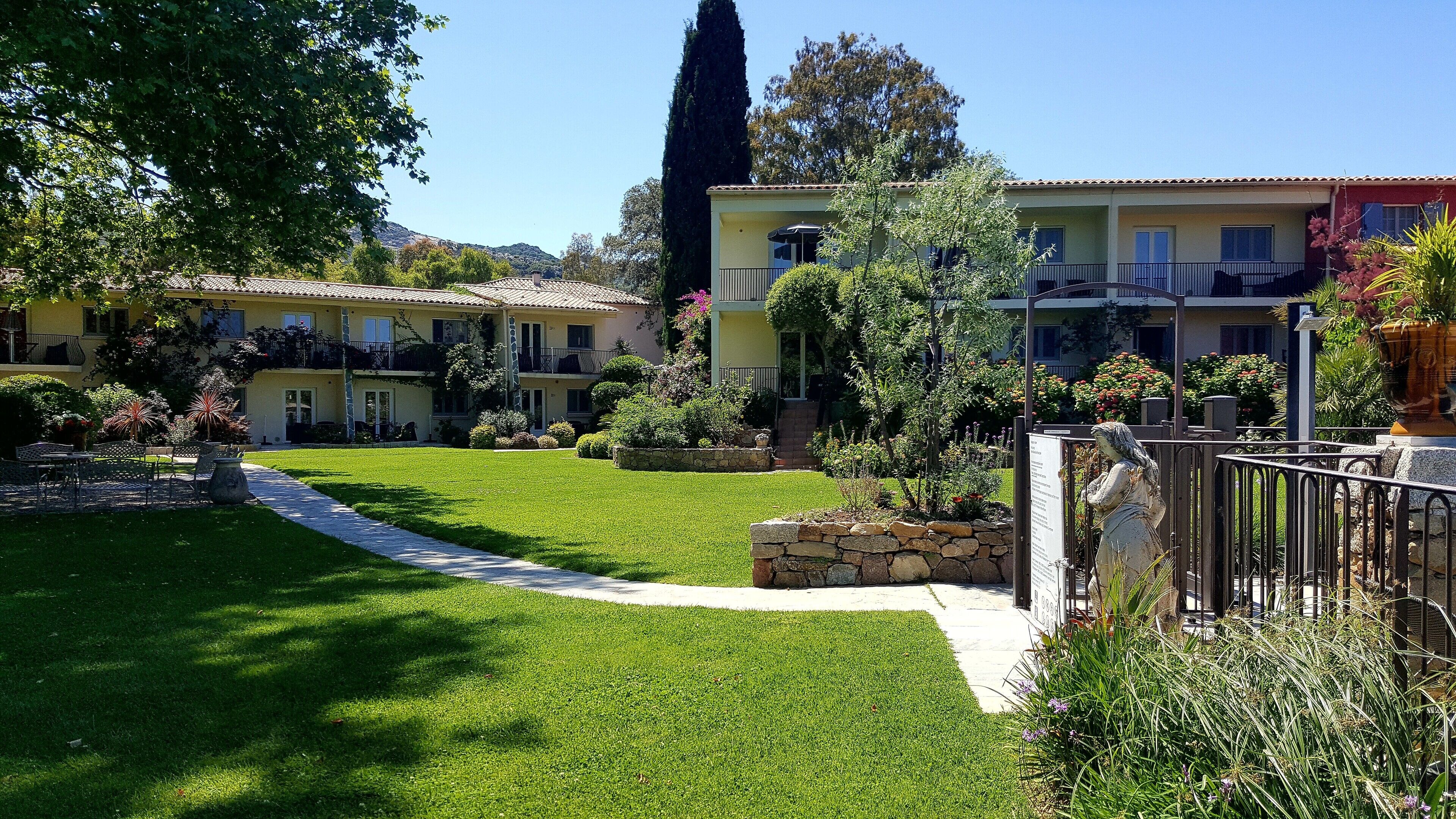 A well-maintained garden with a pathway leading to a building with multiple balconies and a statue.