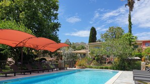 A swimming pool with lounge chairs and umbrellas, surrounded by greenery and buildings. - Résidence Le Home (Calvi)