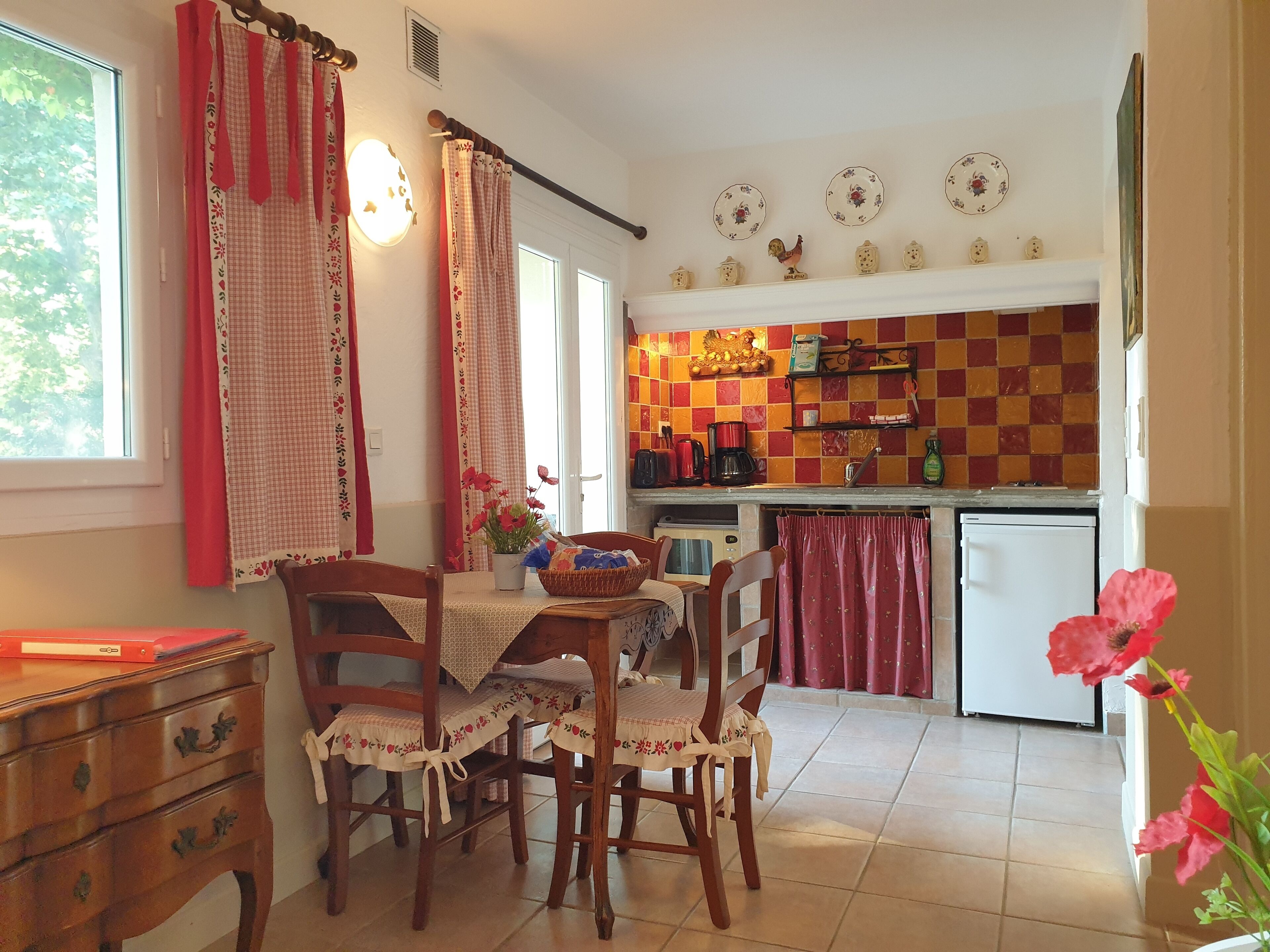 A cozy kitchen with a dining area, featuring a checkered tile backsplash, a refrigerator, and a coffee maker.