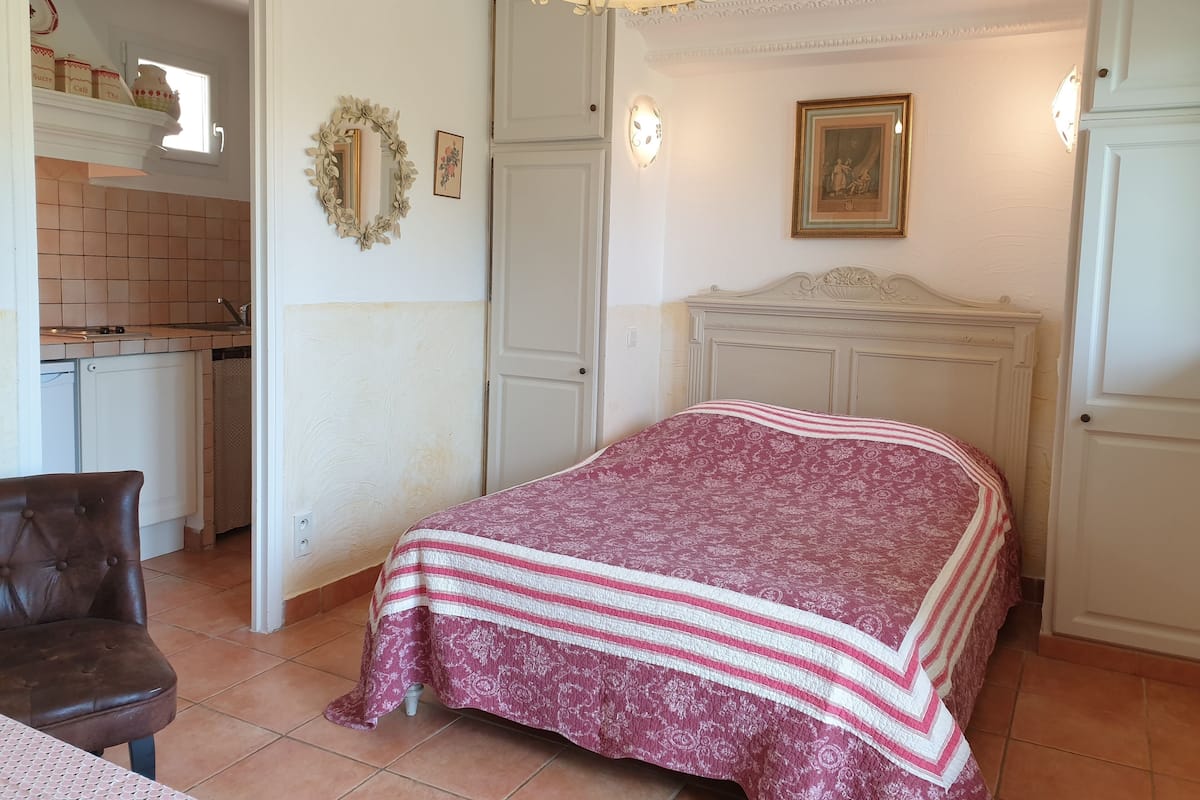 Une chambre comprenant un lit, une chaise, une commode et un petit coin cuisine.