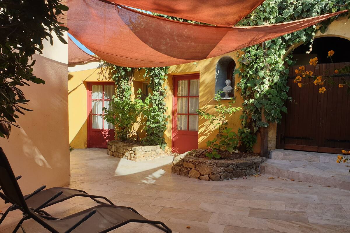 Une cour avec une porte rouge, une statue et une chaise placée sous un auvent.